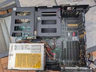 An IBM 5170 PC/AT with its cover off, seen from above: the power supply with its yellow warning label, the drive cage, and the system board with rows of memory chips and expansion slots