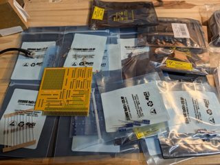Anti-static bags of components, capacitors, resistors and a yellow 8-bit ISA prototype board spread on a wooden bench